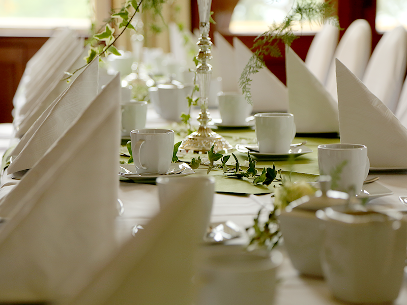 festlich gedeckter Tisch mit weißem Geschirr, grünem Tischläufer, Efeu