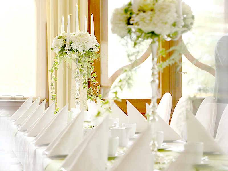 festlich gedeckter Tisch mit weißem Geschirr, Kerzenleuchter mit weißem Blumenschmuck
